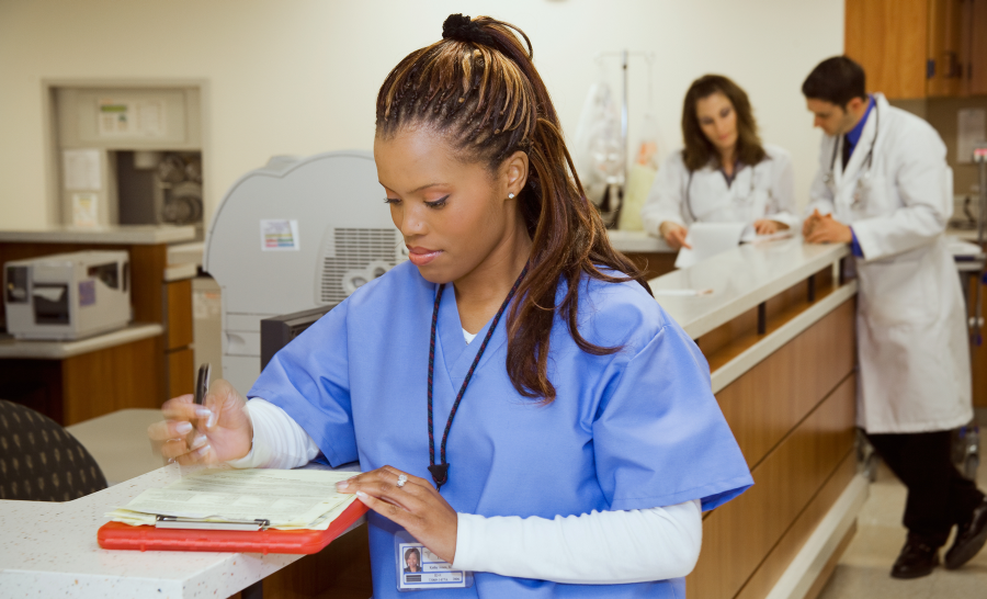 Black female nurse reviewing patient chart at nurses' station in hospital