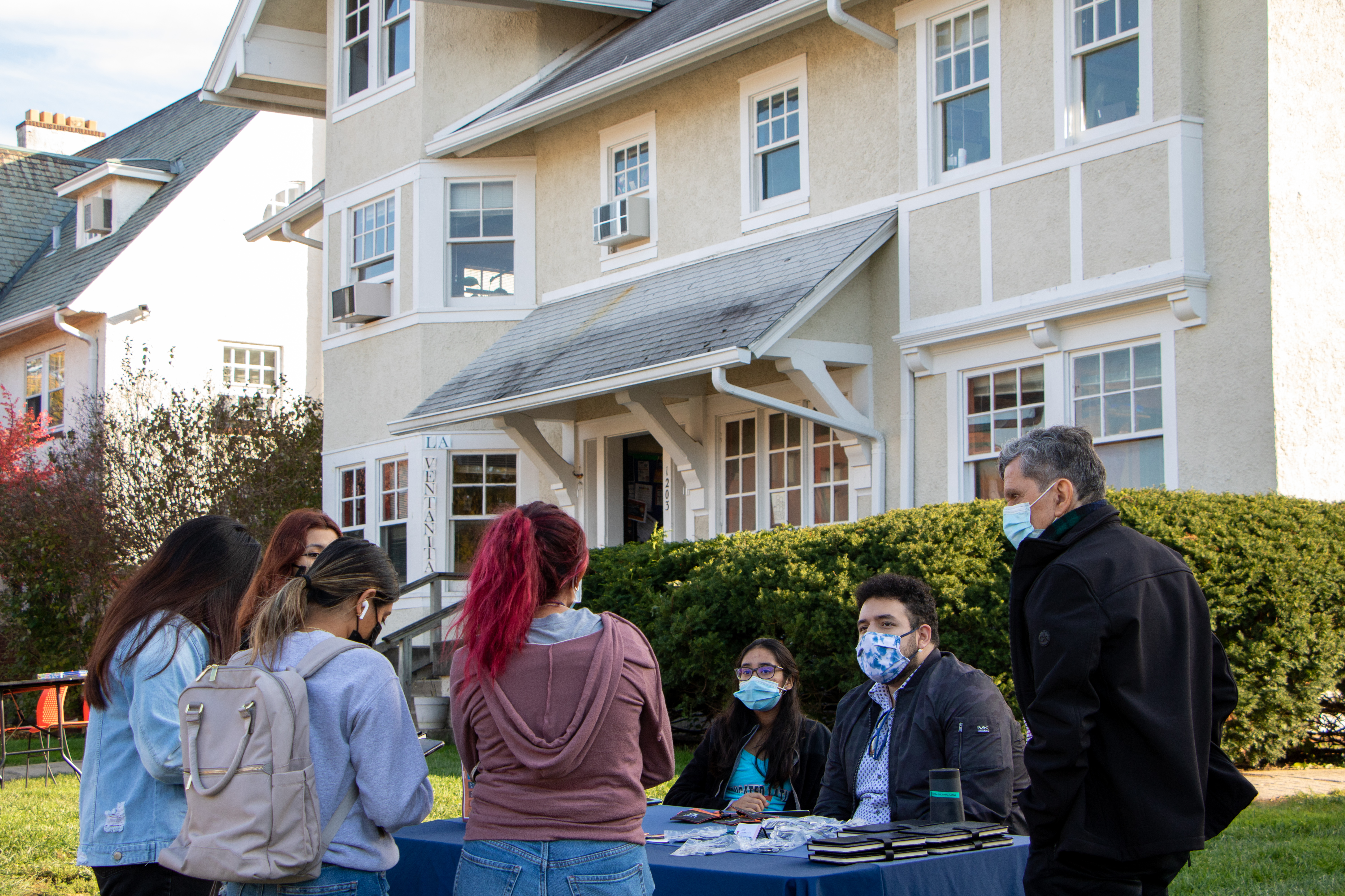 People wearing medical masks standing around table outside of house giving away swag