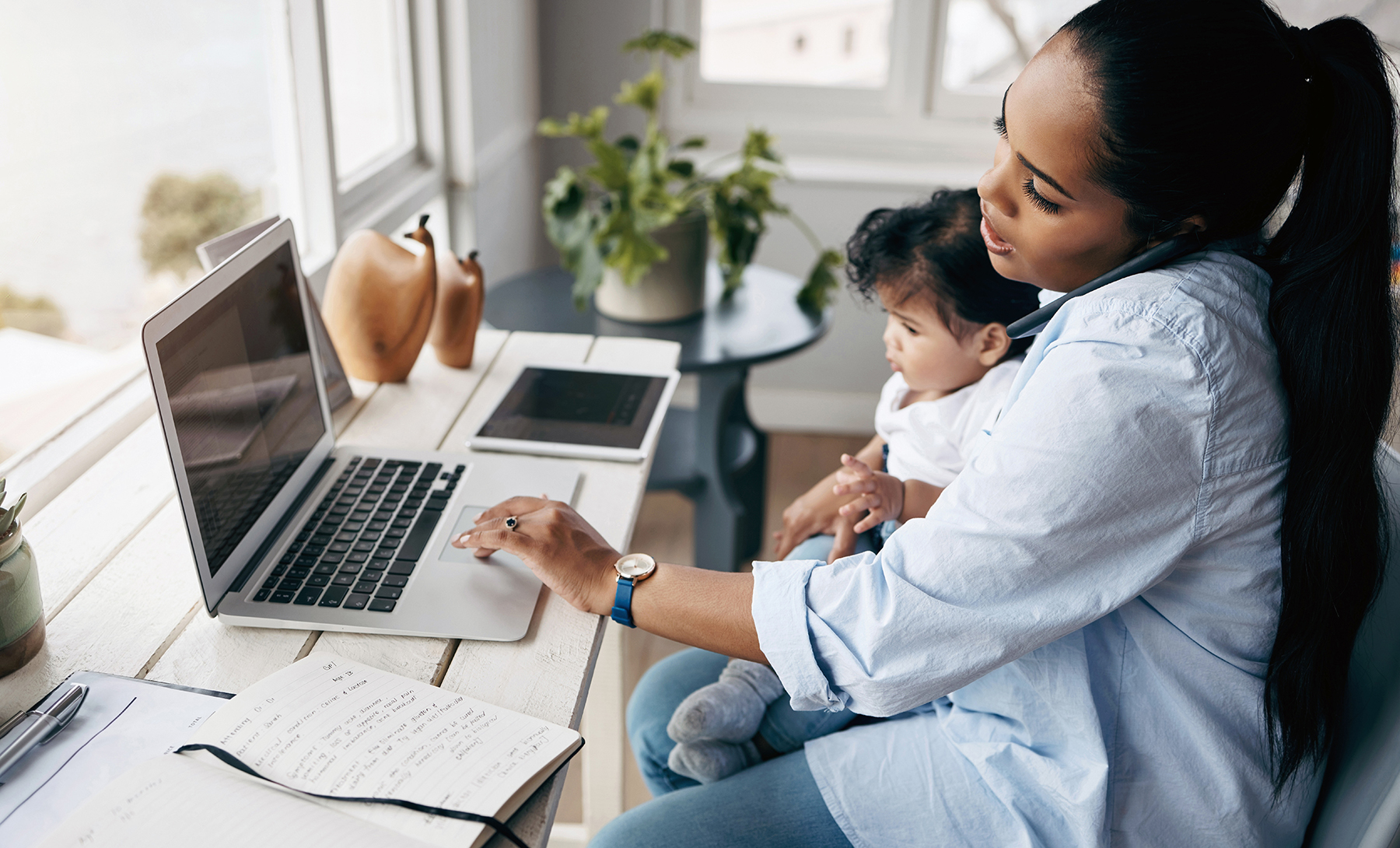 Mother working at laptop while holding baby