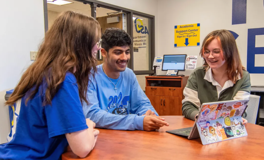 Angelo State Students Sitting around table with laptop with many stickers in first-generation student center
