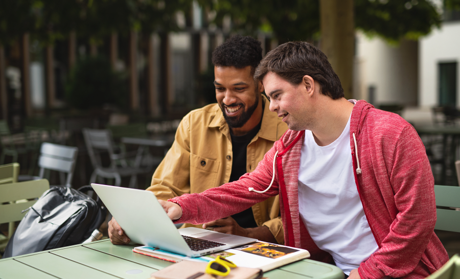 Black male student and white male student with down syndrome working on laptop outside