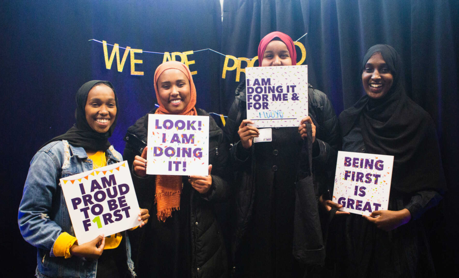 Student group posing with signs expressing first-gen pride with gold letters reading 