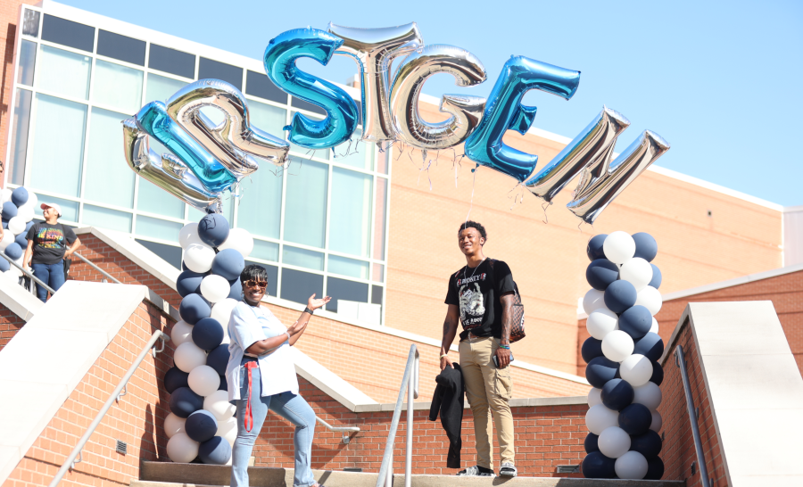 Jackson State Staff member and student posing below blue, white, and silver balloon arch spelling 