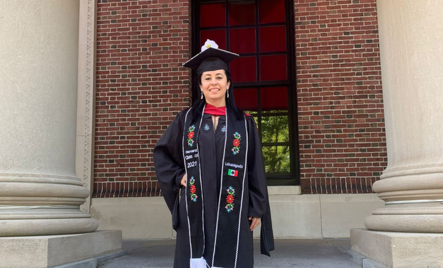 Latina College Graduate standing on steps outside of brick building in cap and gown