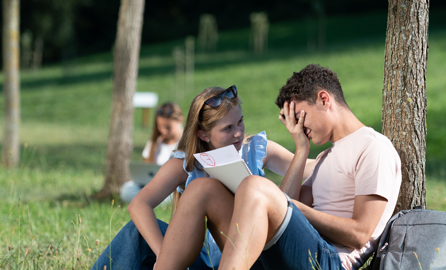 Female student comforting crying male student holding failing paper outside