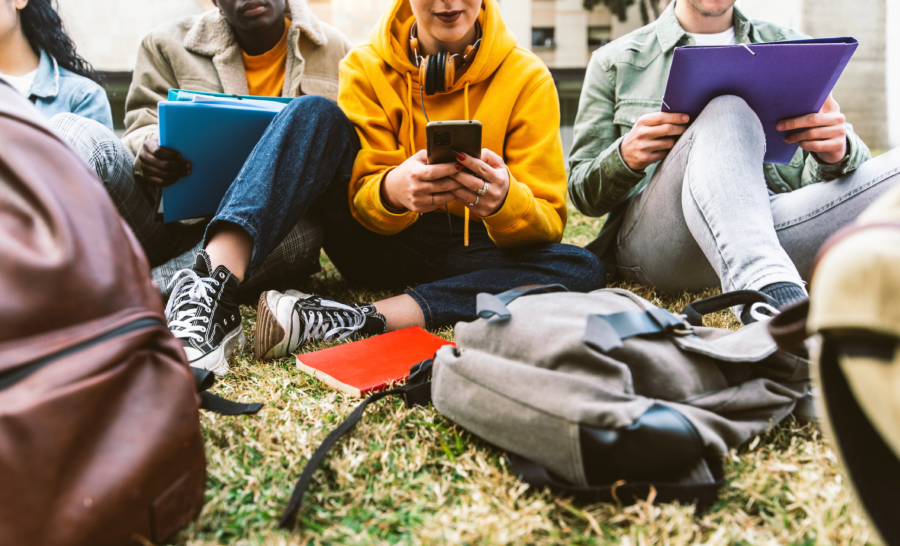 students sitting outside with notebooks and phones