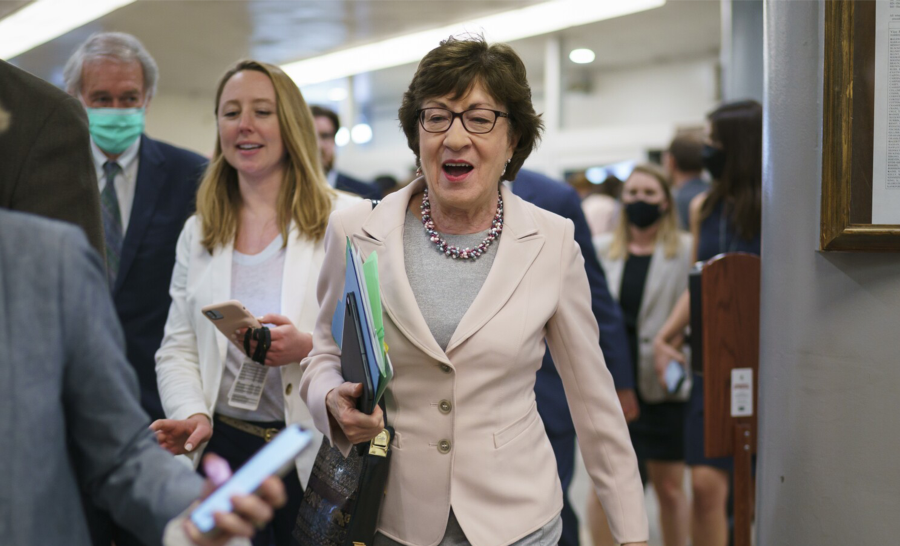 Senator Susan Collins walking down a hallway surrounded by staff
