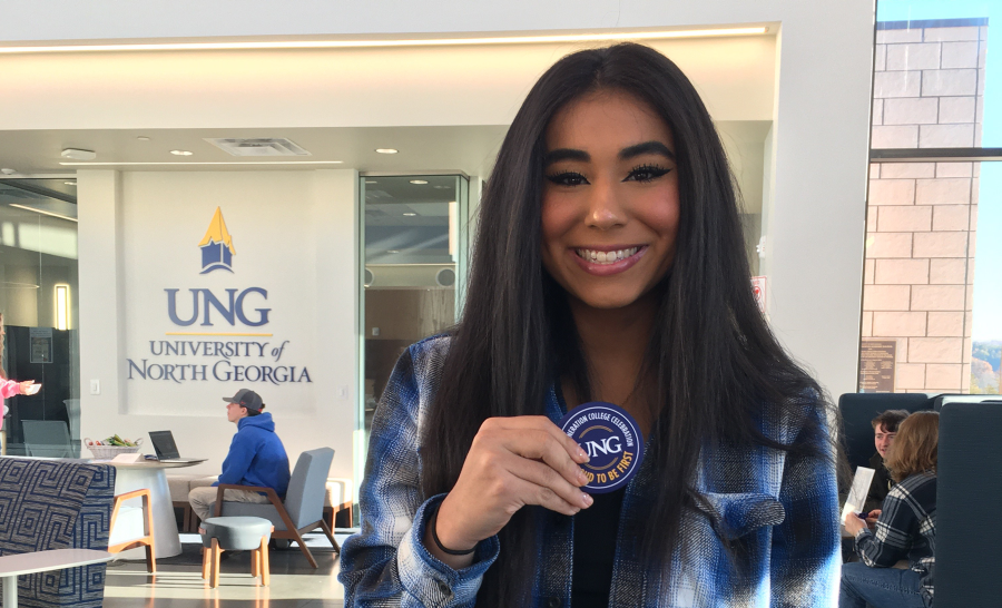 UNG Student holding First-gen sticker in front of UNG logo in student center