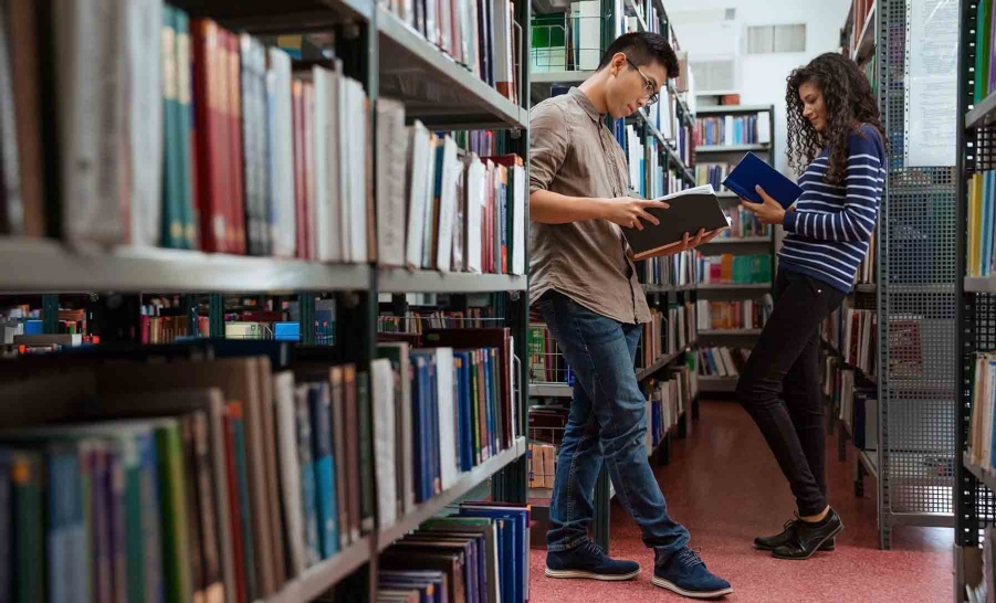 two students standing and reading in library